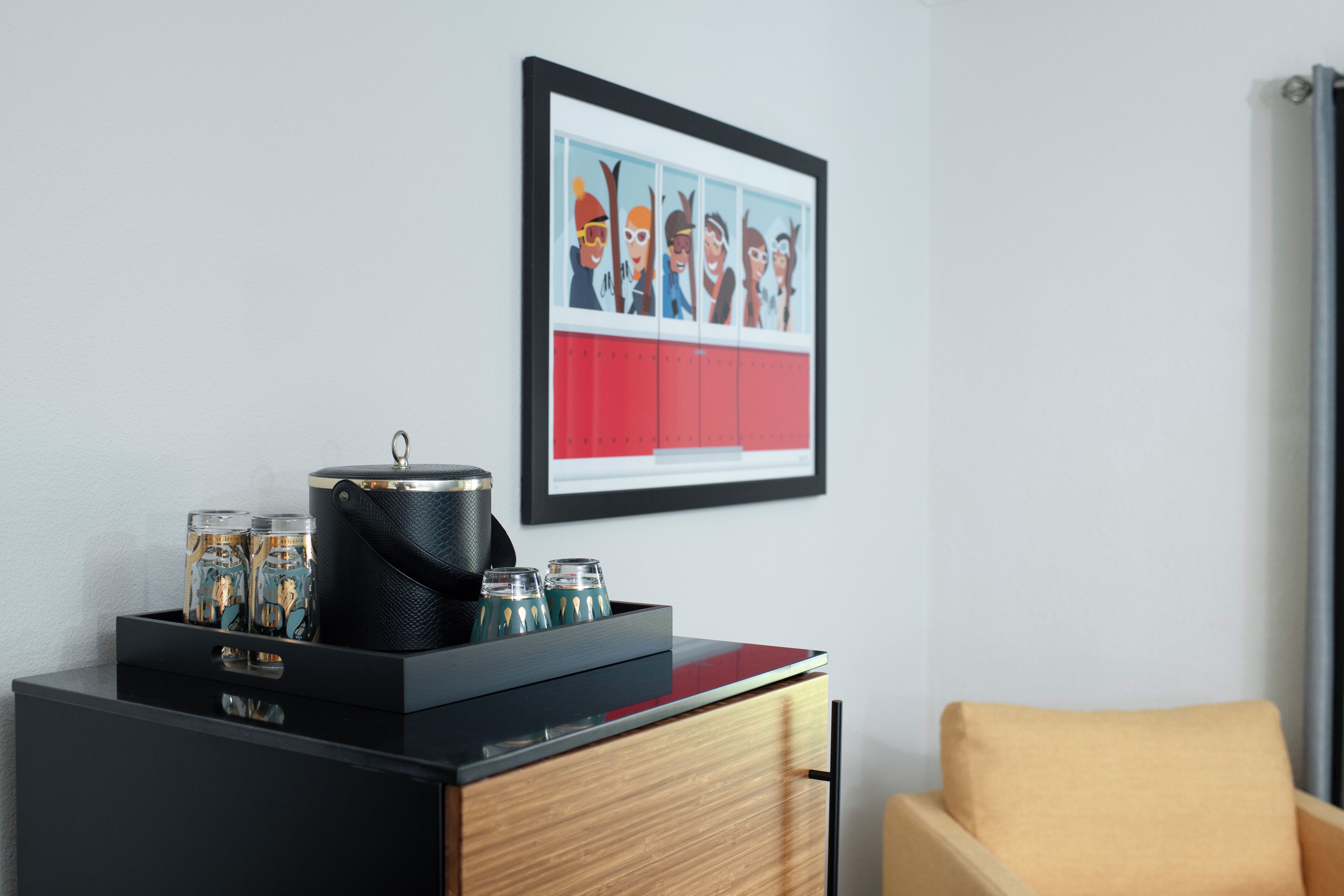 Une chambre d’hôtel moderne avec une commode noire en bois, une œuvre d’art encadrée de style bande dessinée et un fauteuil jaune.