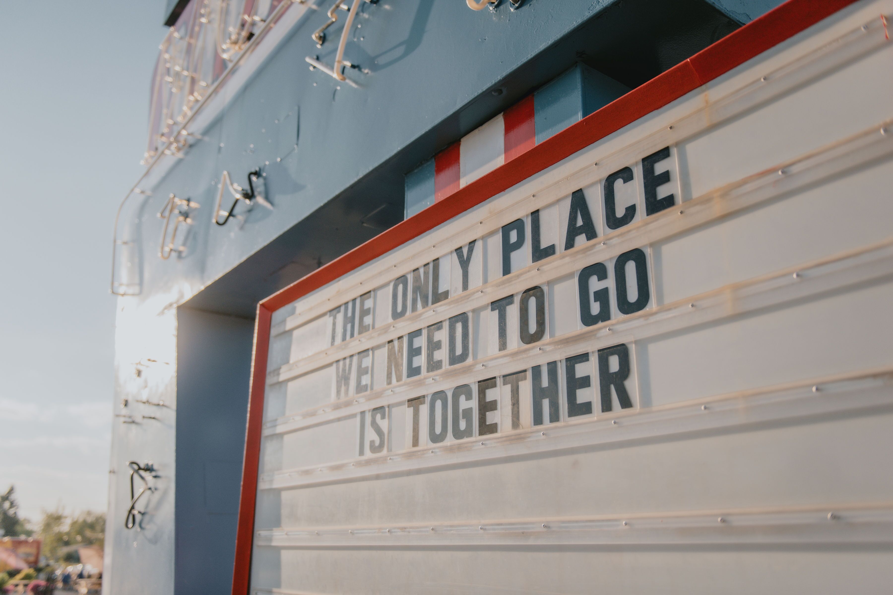Ein Schild mit dem Aufdruck 'THE ONLY PLACE WE NEED TO GO IS TOGETHER' vor weißem Hintergrund mit roten und blauen Streifen.