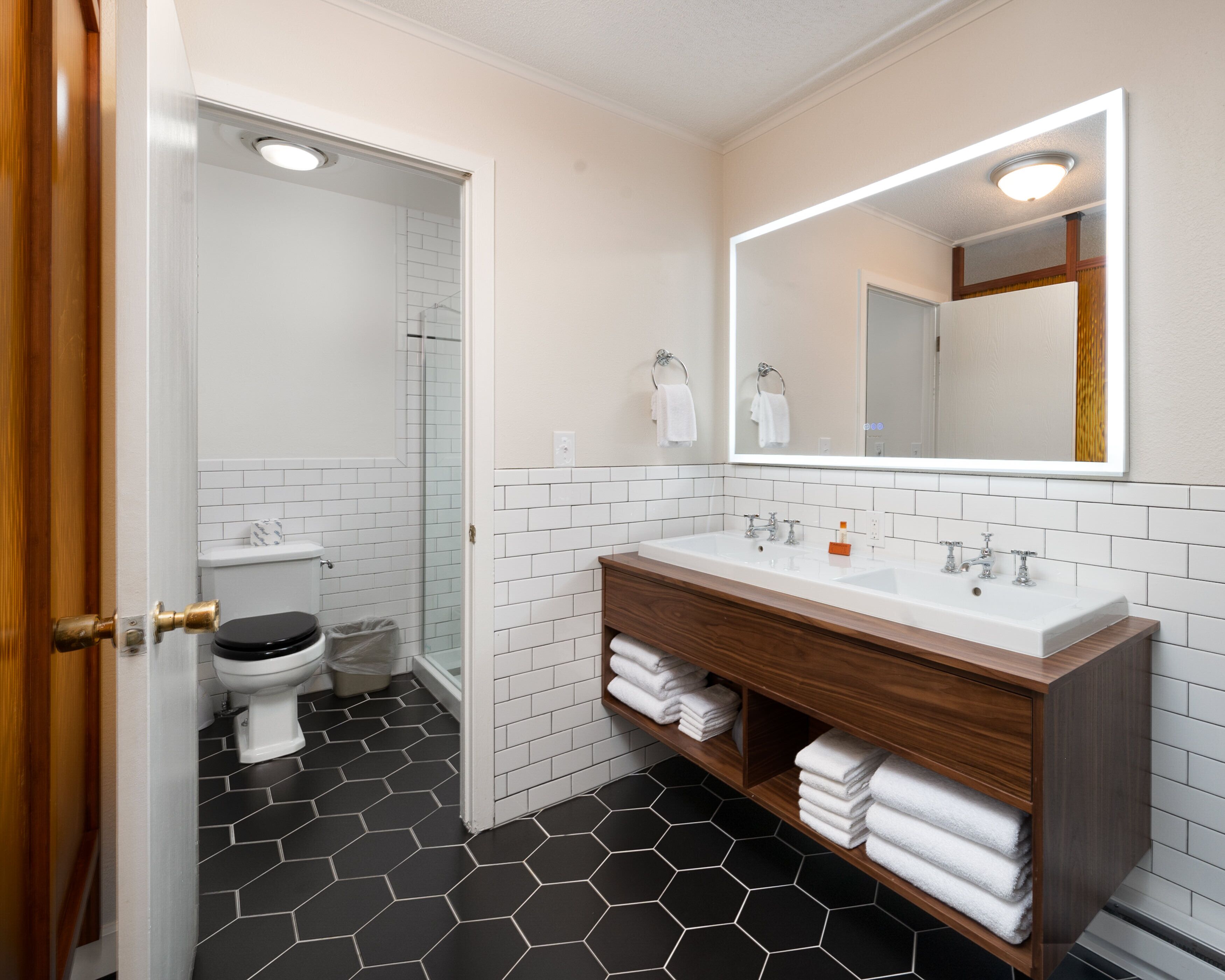 Un baño con inodoro blanco, lavamanos con espejo y ducha.