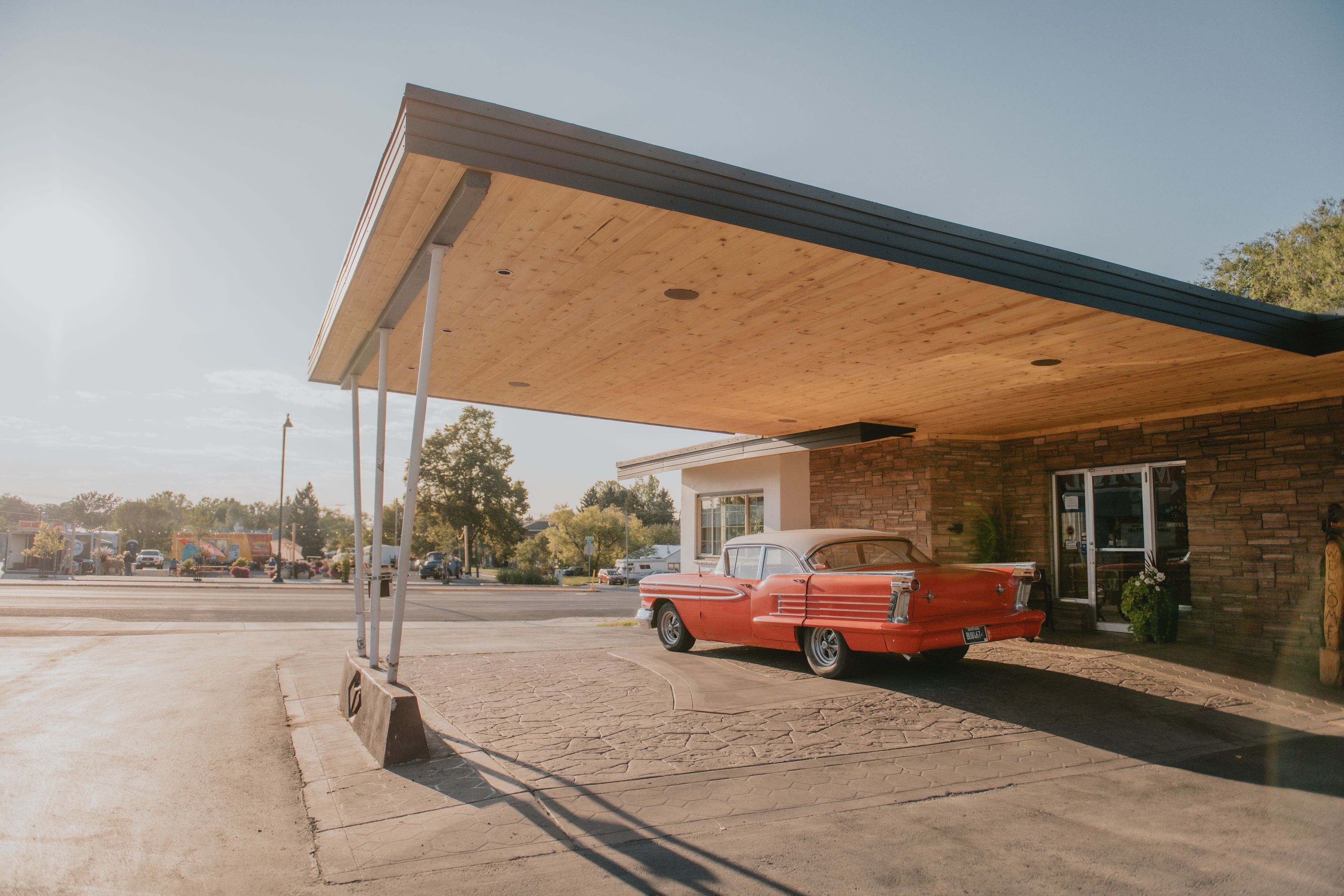 A vintage red car parked under a covered area with a brick building in the background.