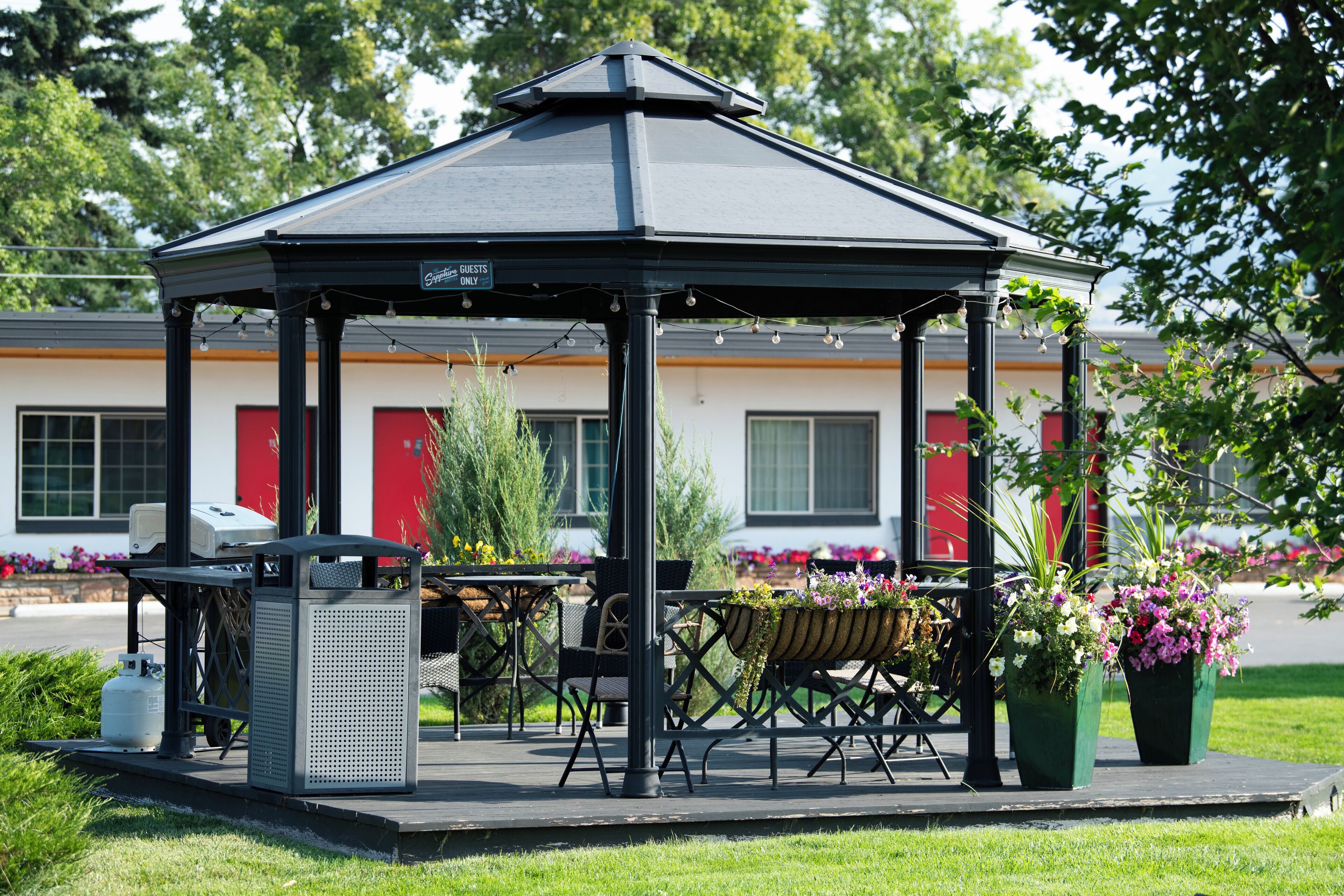 A gazebo with a table and chairs, surrounded by potted plants and flowers.