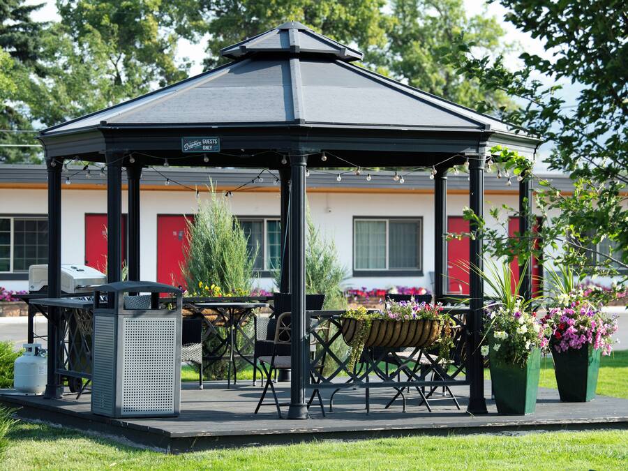 A gazebo with a table and chairs, surrounded by potted plants and flowers.