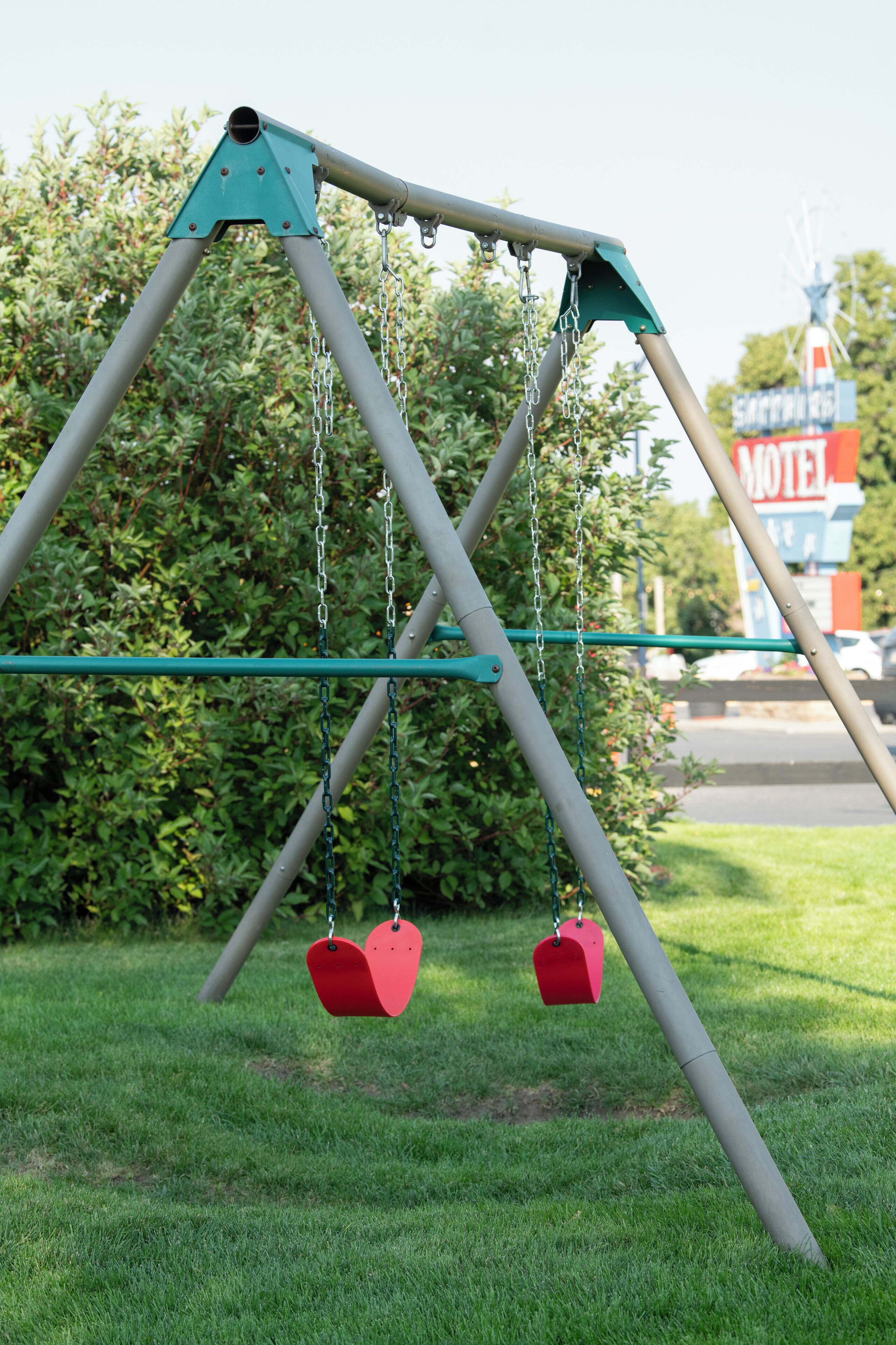 A swing set with two red seats, a motel sign in the background, and a grassy area.