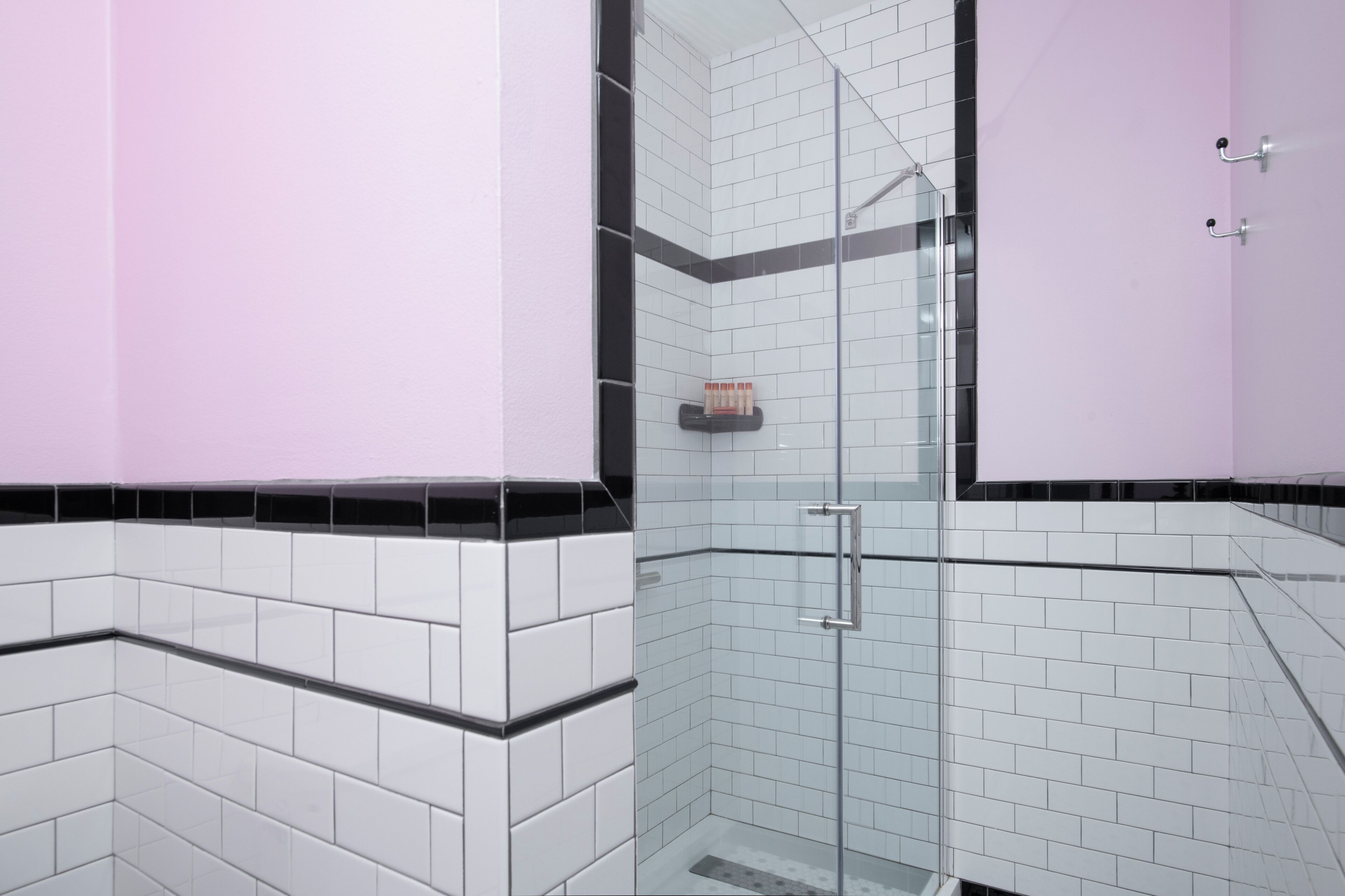 Une salle de bain moderne avec des murs carrelés en noir et blanc, une douche en verre et un mur d’accent rose.