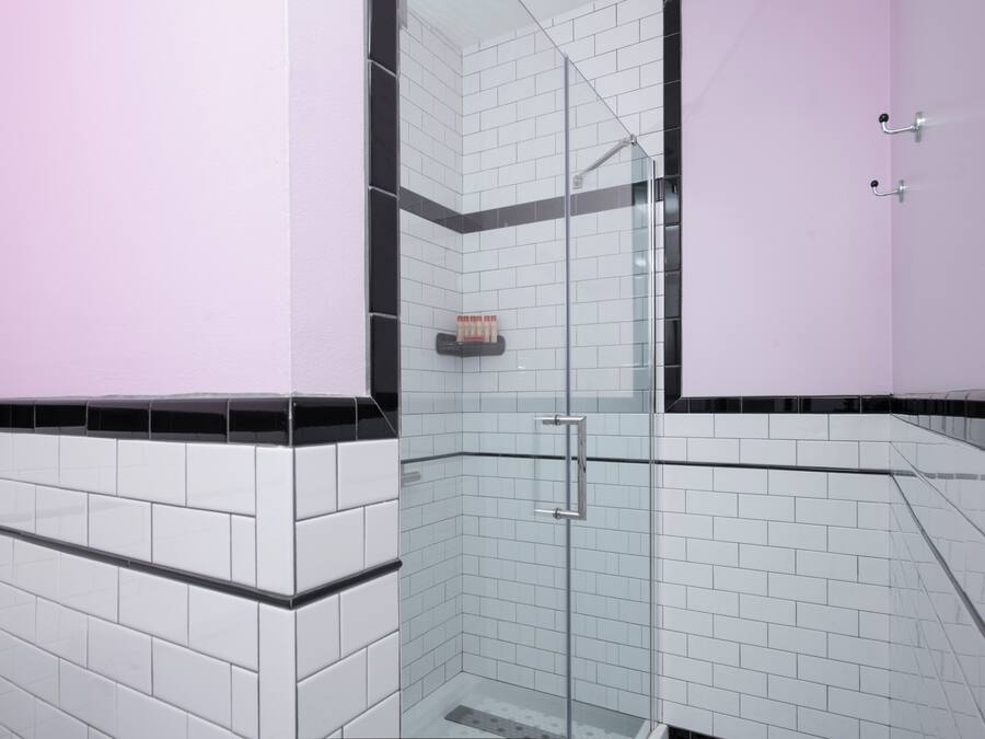 Une salle de bain moderne avec des murs carrelés en noir et blanc, une douche en verre et un mur d’accent rose.