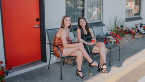 Two women sitting on outdoor chairs in front of a building with a red door and a window. - The Sapphire Motel (Bozeman)