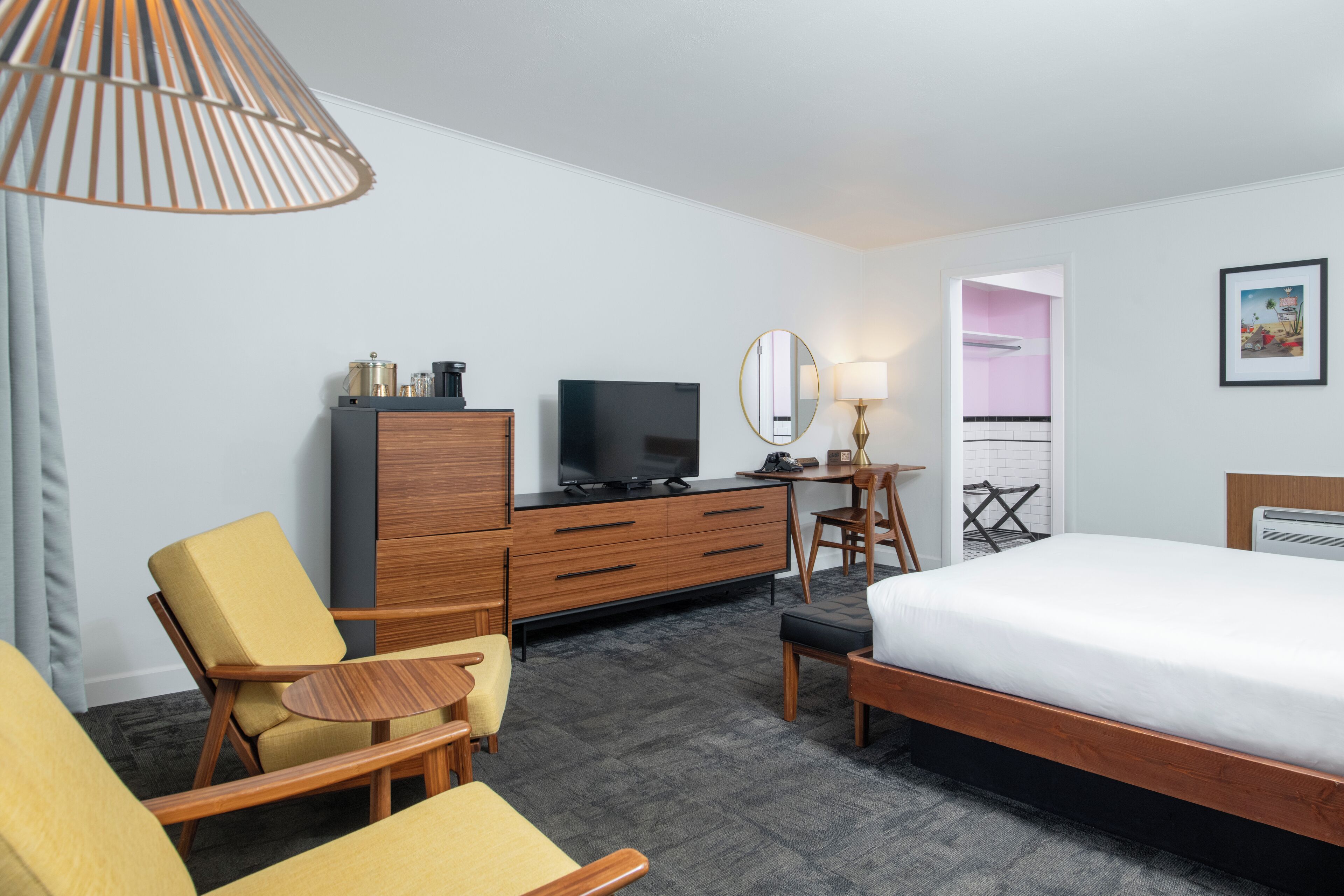 A hotel room with a bed, a TV, a desk, a chair, a lamp, and a wardrobe.