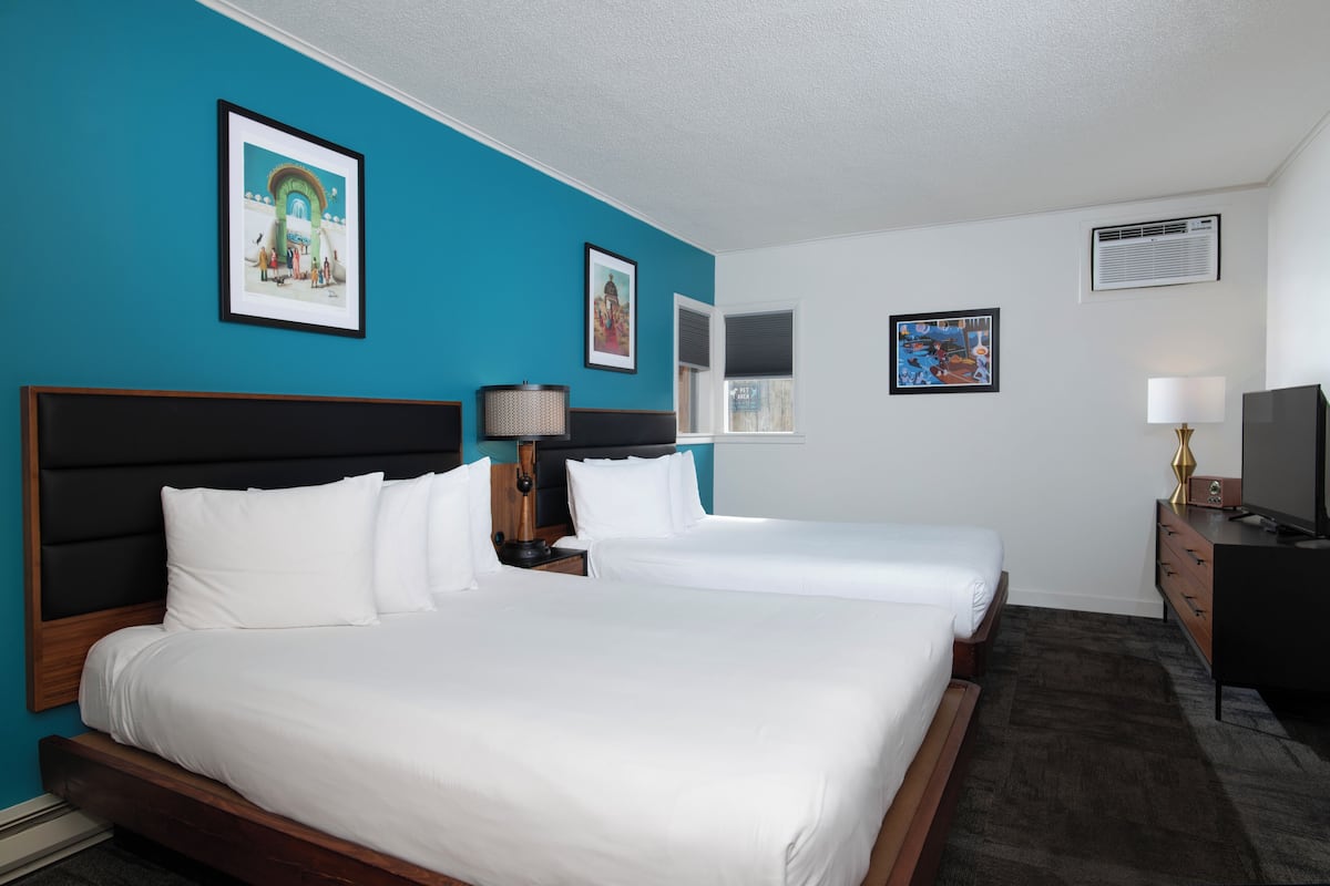 A hotel room with two beds, a TV, a lamp, and artwork on the walls.