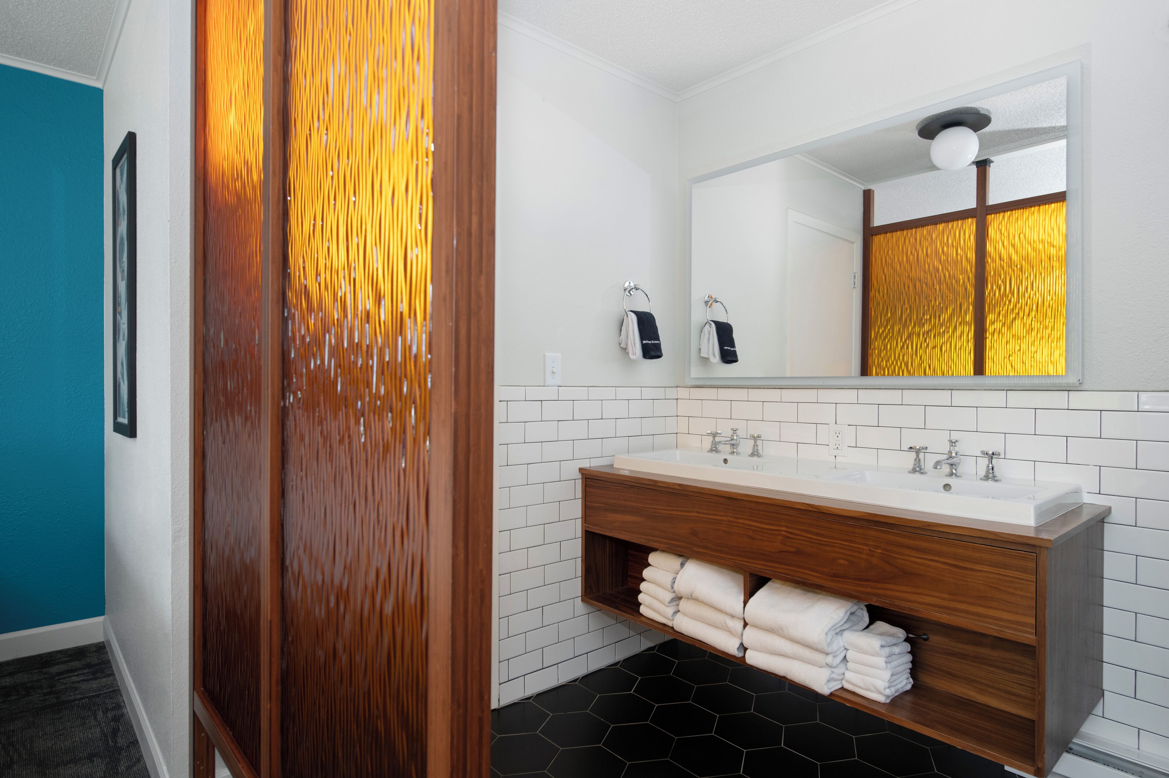 A modern bathroom with a wooden vanity, white subway tiles, a large mirror, and a black hexagonal floor.