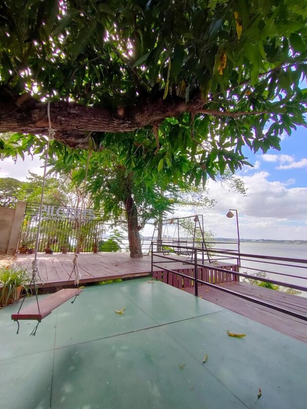 A wooden deck with a view of a body of water, surrounded by greenery and a metal railing.