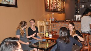 Un grupo de personas sentadas alrededor de una mesa en un restaurante con paredes de ladrillo y una pizarra con el menú.