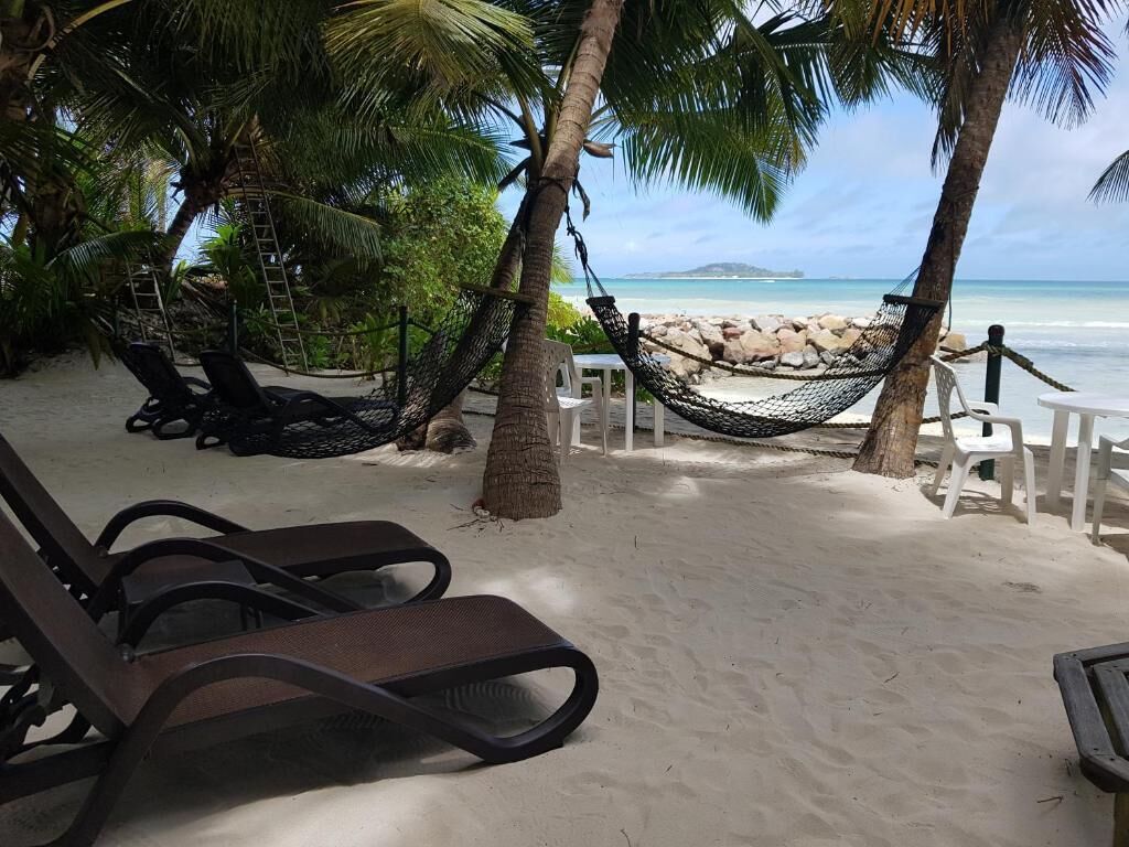 Cenário de praia com uma rede, cadeiras de descanso e vista para o oceano.