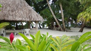 A beachside hut with a thatched roof, surrounded by palm trees and a sandy beach. - Anse Kerlan Beach Chalets (Praslin Island)