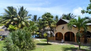 A resort with a central building featuring arched doorways, surrounded by lush palm trees and a well-maintained lawn. - Anse Kerlan Beach Chalets (Praslin Island)
