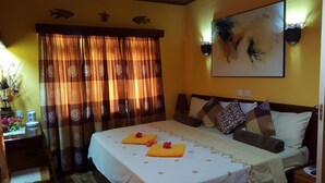 A hotel room with a bed, curtains, a painting, and a bedside table with a lamp. - Anse Kerlan Beach Chalets (Praslin Island)