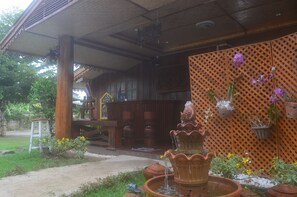 A wooden building with a covered porch, a tiered water fountain, and potted plants.