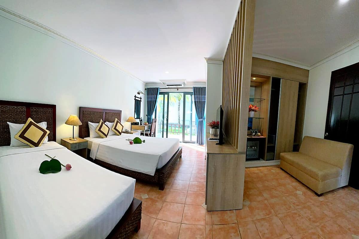 A hotel room with two beds, a sofa, a TV, and a balcony with curtains.