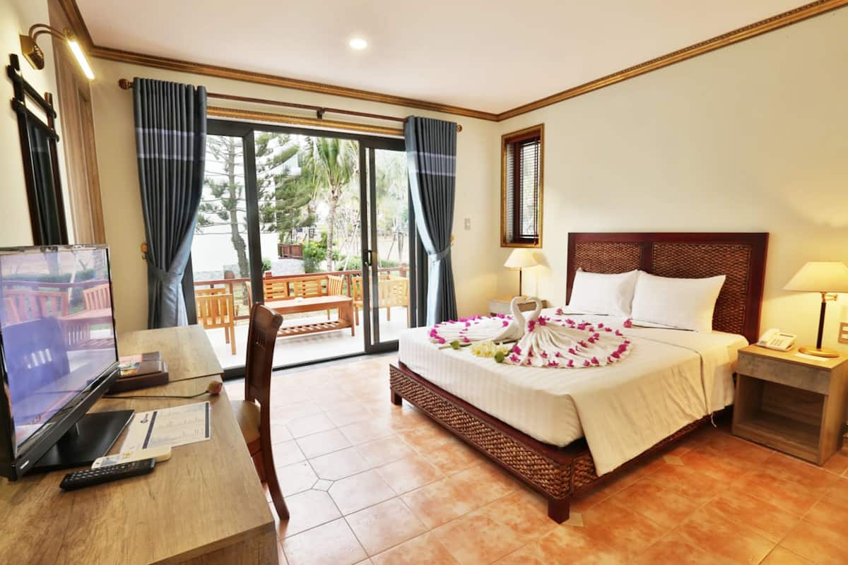 A hotel room with a bed, a desk with a TV, a chair, and a balcony with a table and chairs.