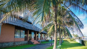 A thatched-roof building with a paved walkway leading to it, surrounded by palm trees and a well-maintained lawn. - Lotus Vung Tau Resort (Ho Chi Minh City)