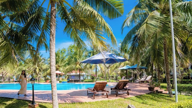 A poolside area with lounge chairs, umbrellas, and palm trees. - Lotus Vung Tau Resort (Ho Chi Minh City)
