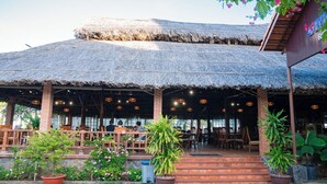 A restaurant with a thatched roof, outdoor seating, and potted plants. - Lotus Vung Tau Resort (Ho Chi Minh City)