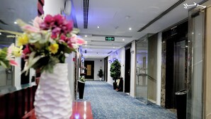 A hotel corridor with a blue marble floor, potted plants, and a reception area with a white vase of flowers. - Merfal Serviced Apartments-Royal (Riyadh)