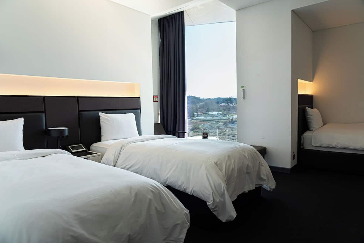 A hotel room with two beds, a large window, and a view of a cityscape.