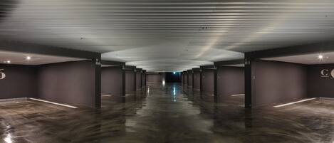 A long, empty corridor with a shiny floor and dark walls, featuring numbered pillars and a ceiling with recessed lighting.