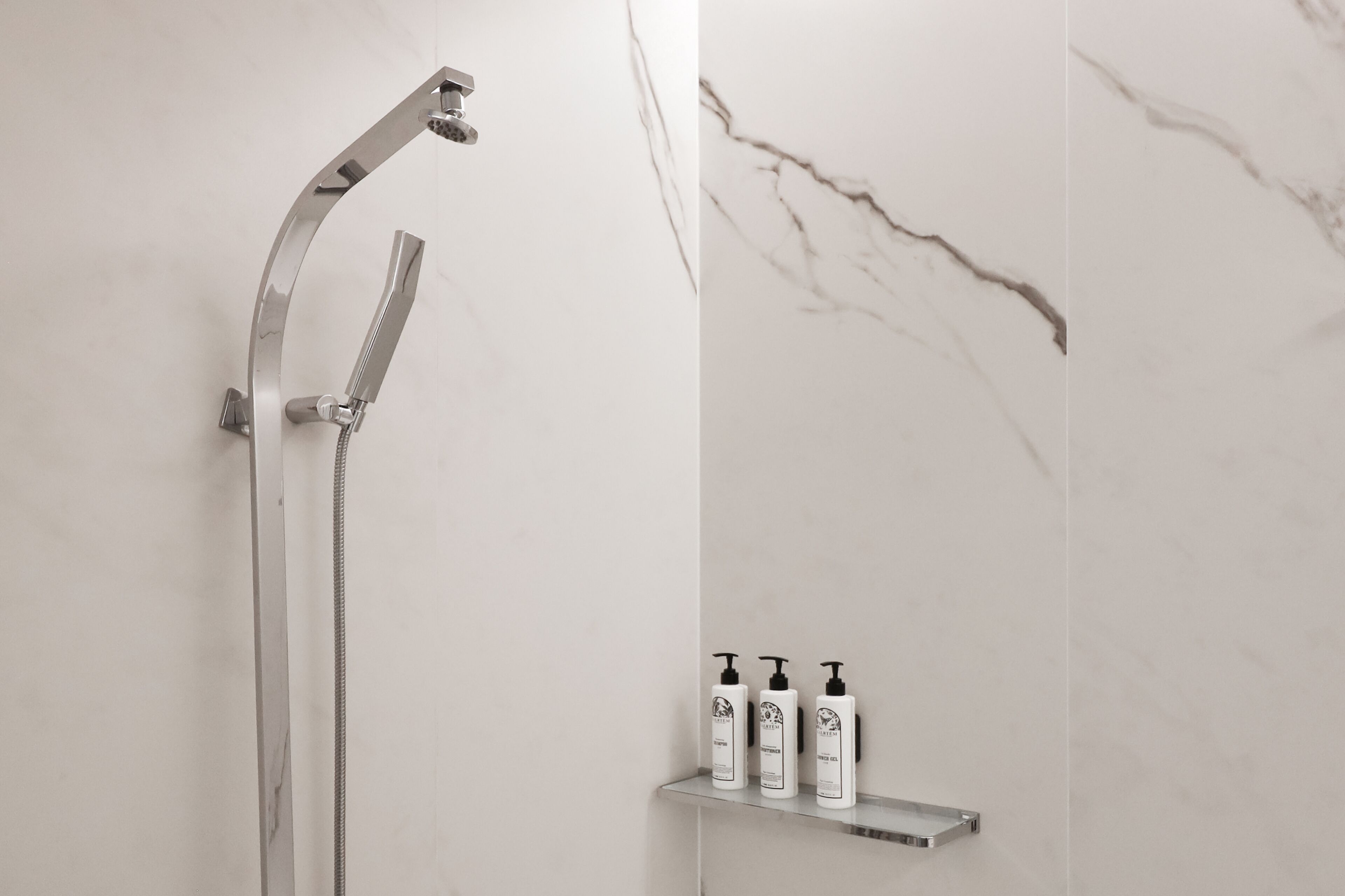 Un baño moderno con ducha, paredes de mármol y un estante con artículos de aseo.