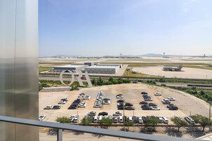 Un parking d’aéroport avec plusieurs rangées de voitures garées et un grand bâtiment en arrière-plan.