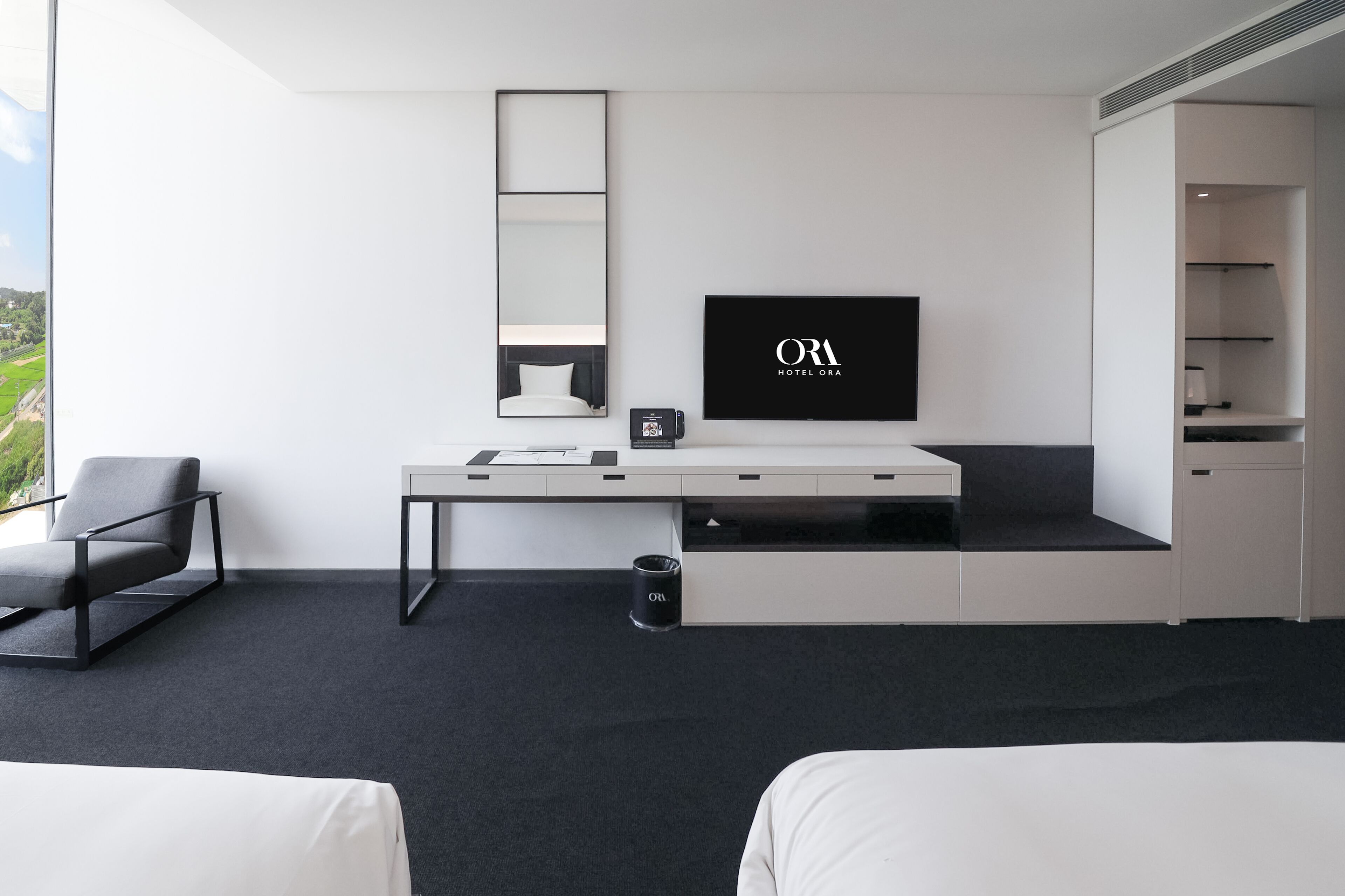 A modern hotel room with a large bed, a desk with a flat-screen TV, a chair, and a view of the outdoors.