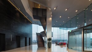 Un vestíbulo amplio con una escalera moderna, paredes de cristal y una planta grande.