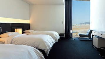 A hotel room with two beds, a desk, a chair, and a view of the airport.