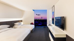 Habitación de hotel con dos camas, televisión y vista de un avión despegando.