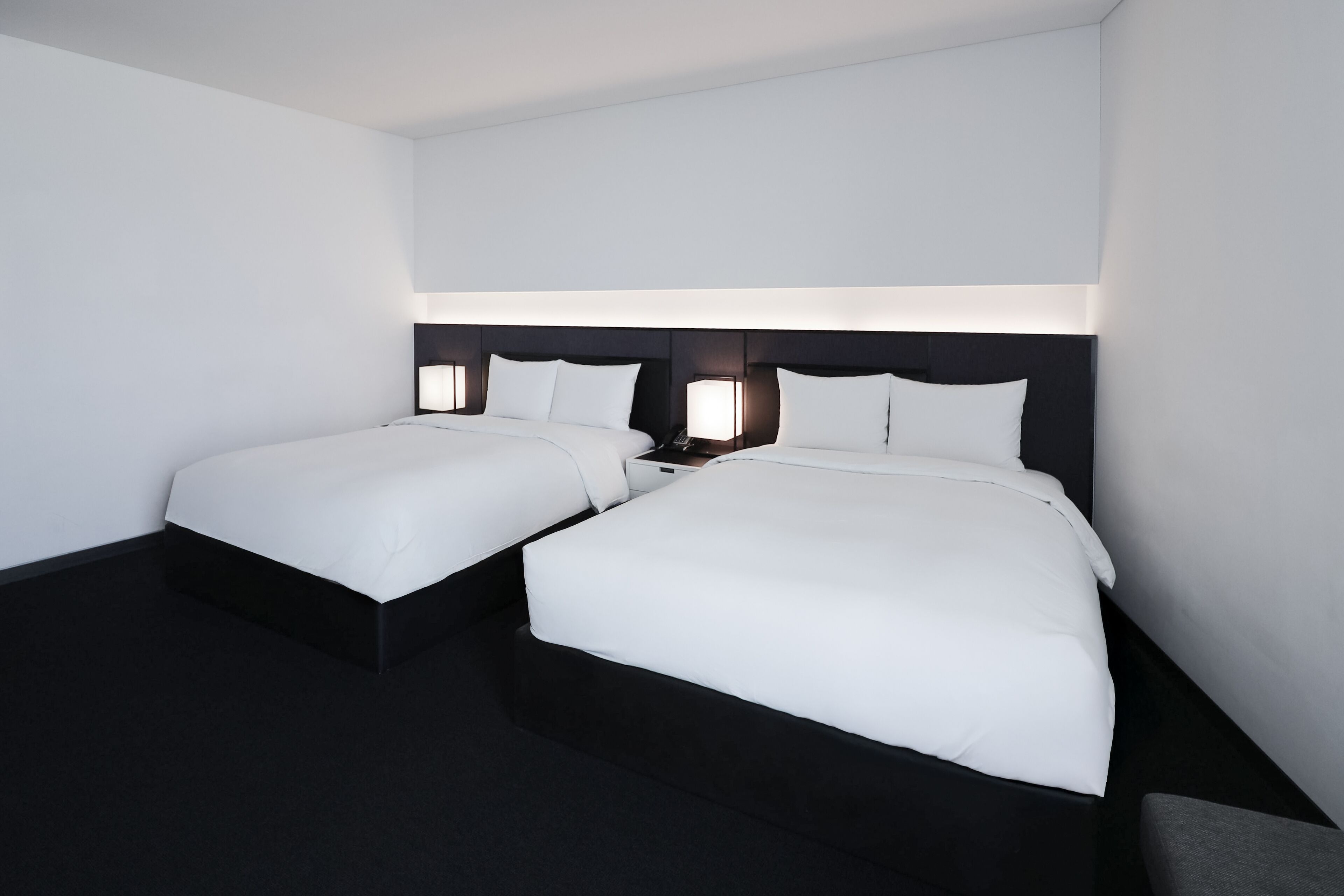 Habitación de hotel con dos camas, cada una con cabecero negro y ropa de cama blanca.