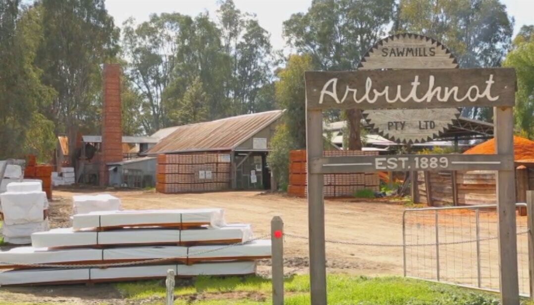 A sign for 'Arbuthtnot Sawmills Pty Ltd' with a rustic wooden structure and a brick chimney in the background.