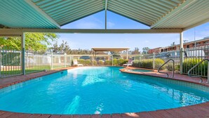 A swimming pool with a covered area, surrounded by a fence, and a view of buildings in the background. - Comfort Inn Clubarham (Barham)