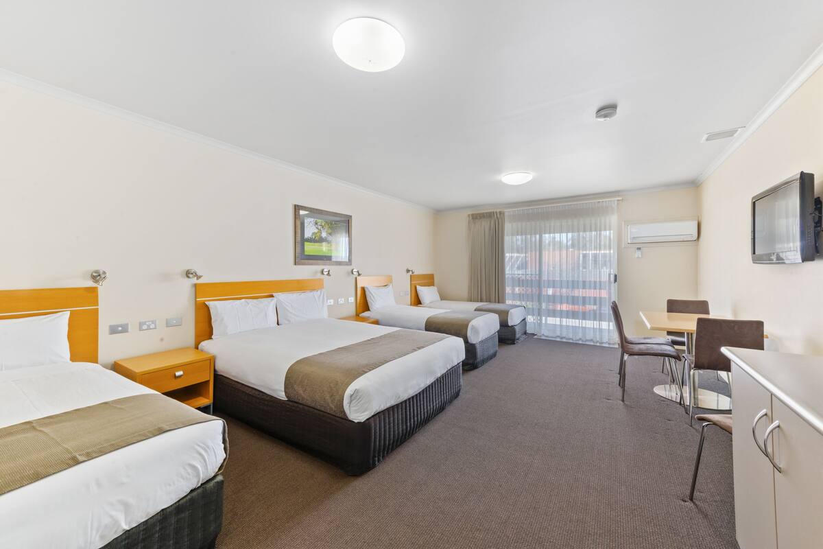 A hotel room with three beds, a desk, and a chair.