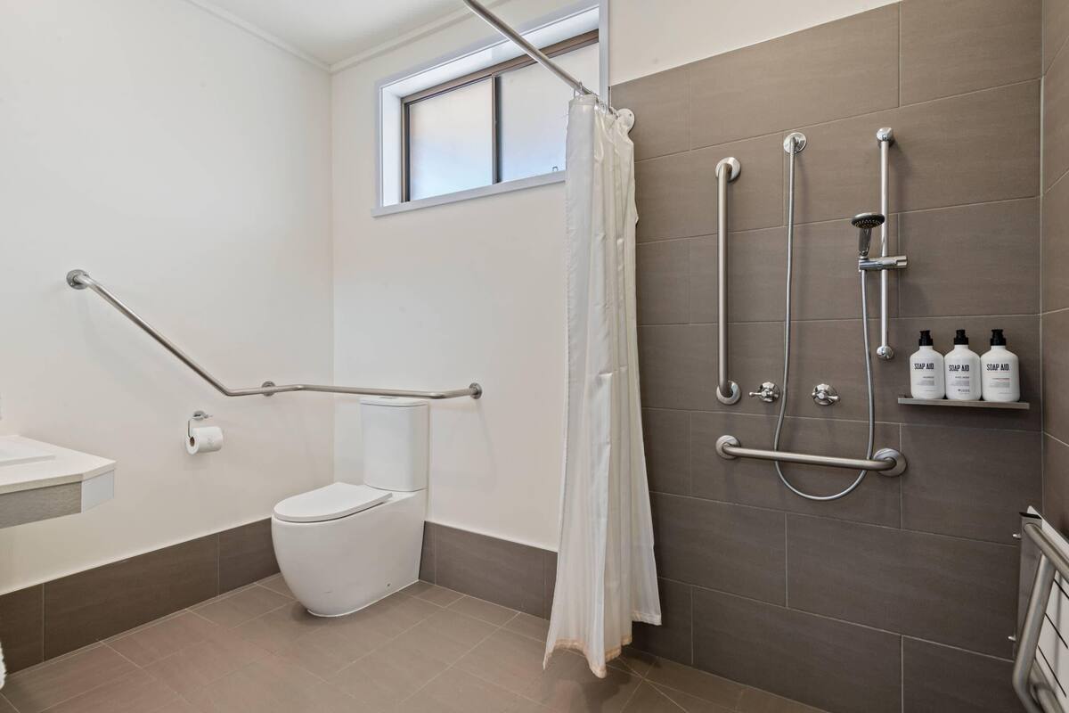 A bathroom with a shower, toilet, grab bars, and soap dispensers.