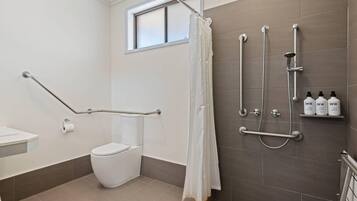 A bathroom with a shower, toilet, grab bars, and soap dispensers.