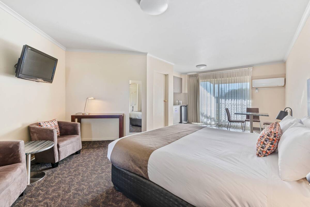A hotel room with a large bed, a desk, a chair, a TV, and a view of the outdoors.