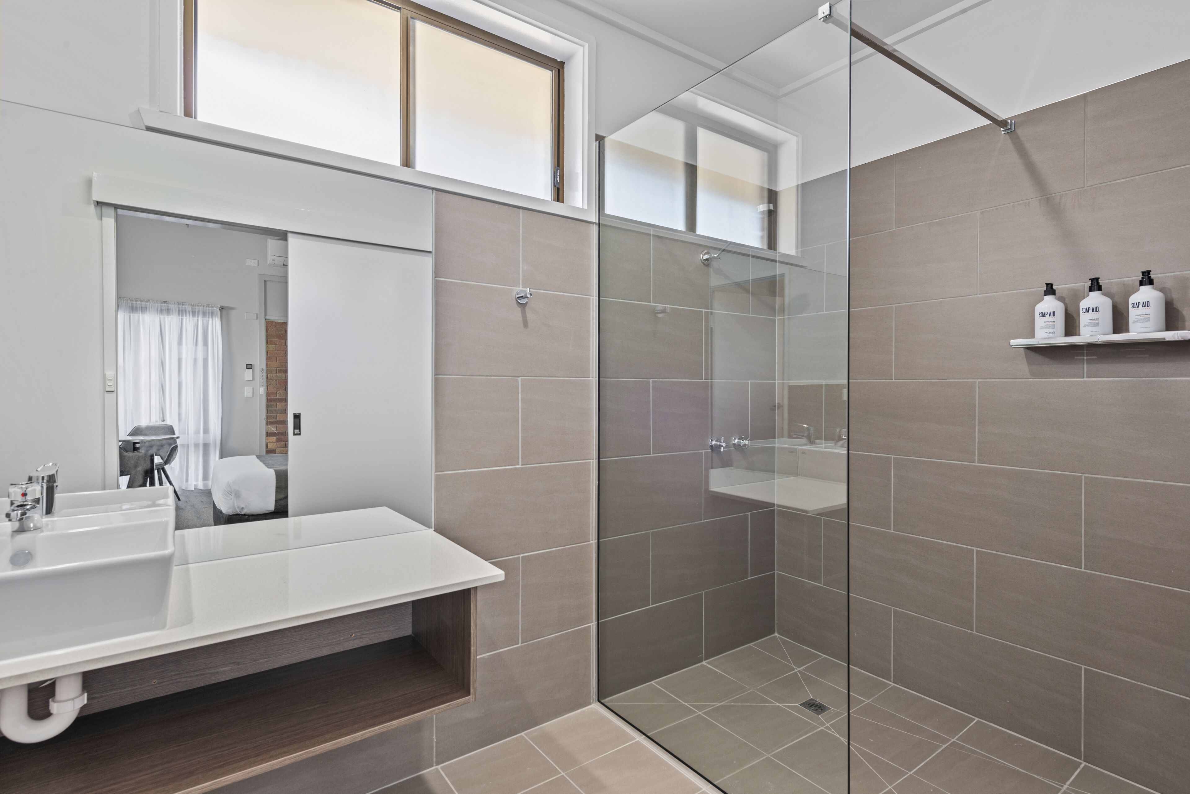 A modern bathroom with a glass-enclosed shower, a large mirror, and a white vanity.