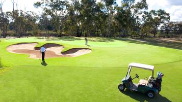 A golf course with a green fairway, sand bunkers, and a golf cart.