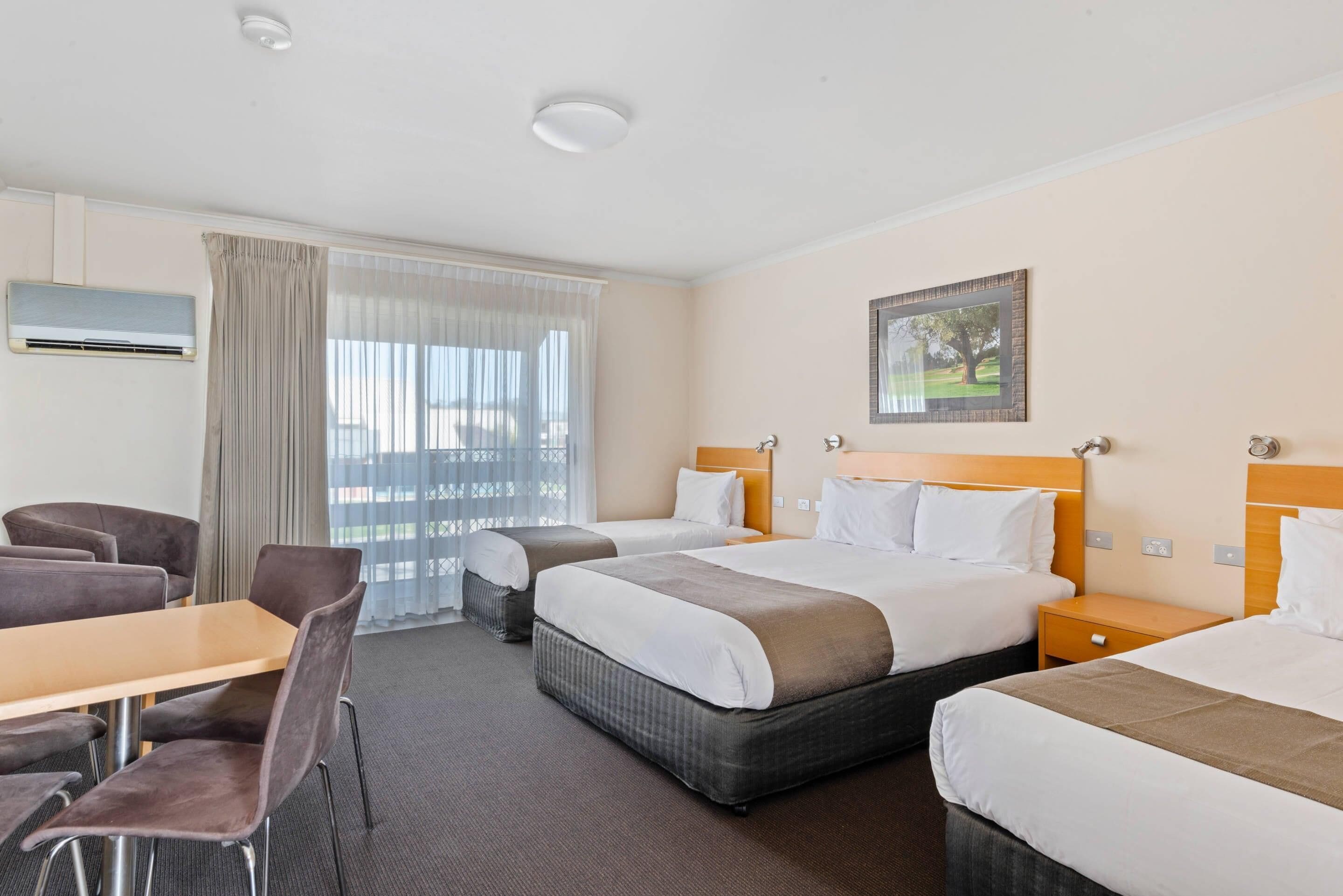 Een hotelkamer met twee bedden, een bureau, stoelen en een raam met gordijnen.