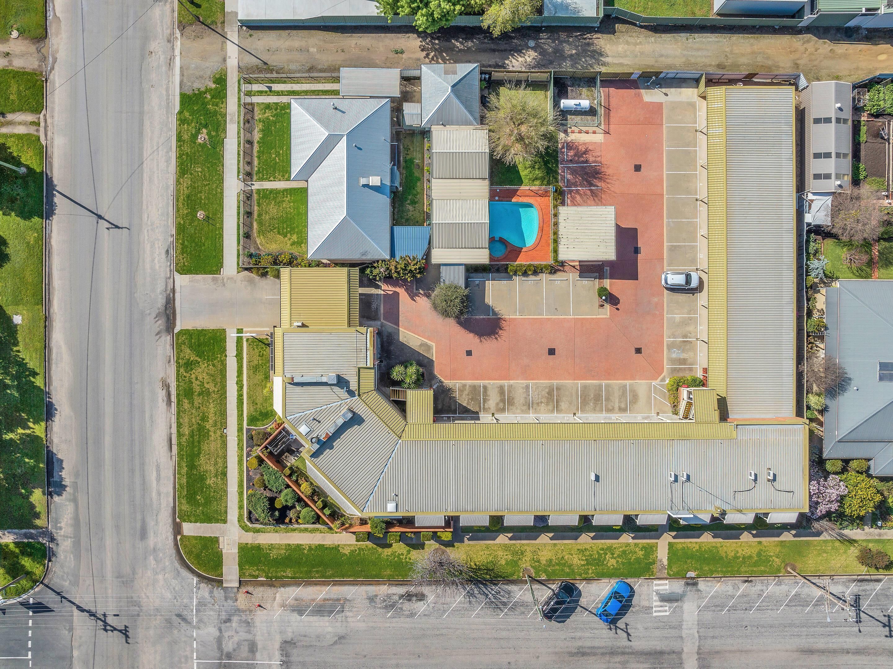 Vista aérea de un edificio comercial con estacionamiento, piscina y una amplia zona cubierta.