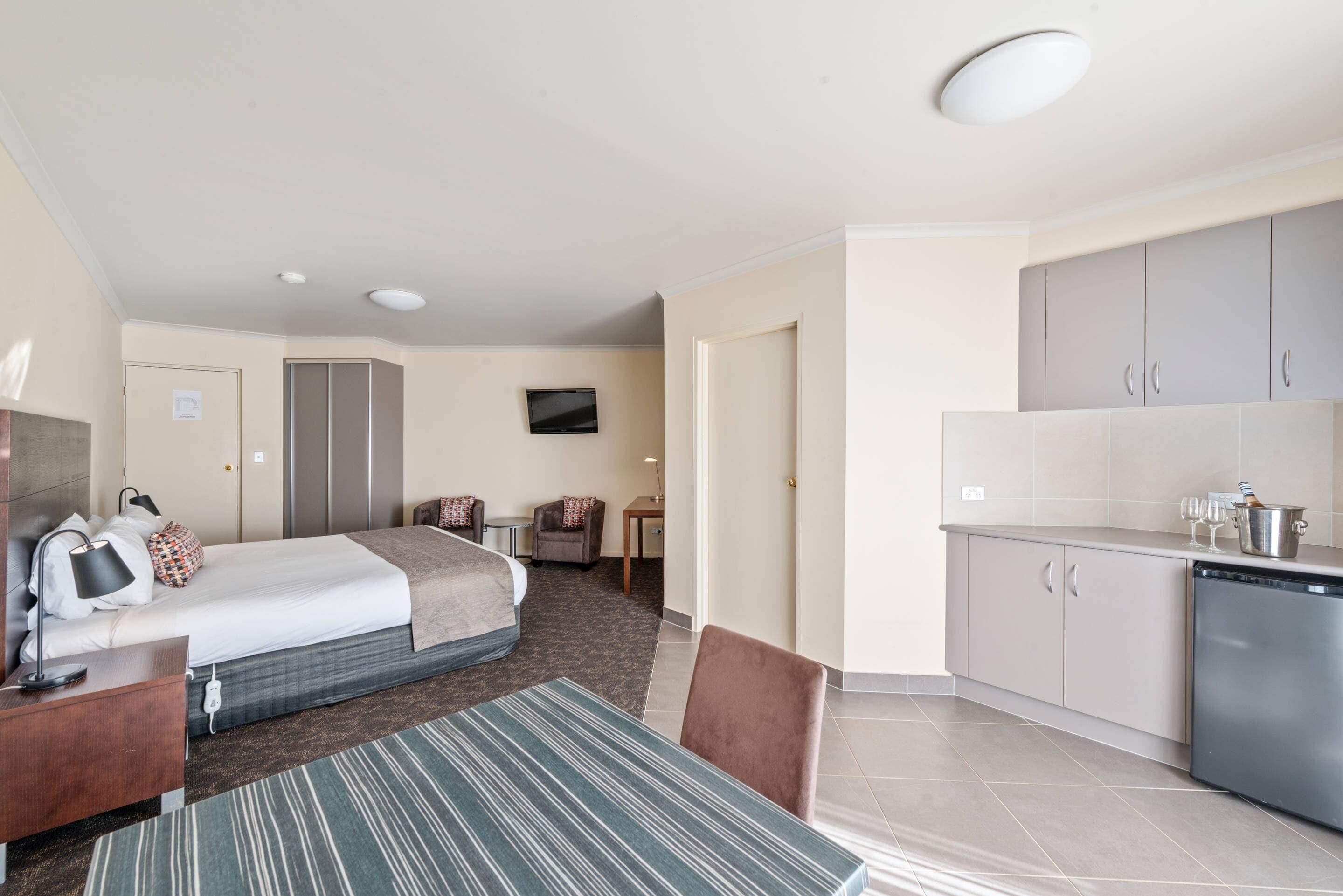 Une chambre d’hôtel comprenant un lit, une table de chevet, une lampe, une chaise et une petite table recouverte d’une nappe à rayures.