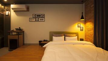 A hotel room with a bed, a small table, a trash bin, and a wall-mounted air conditioner.