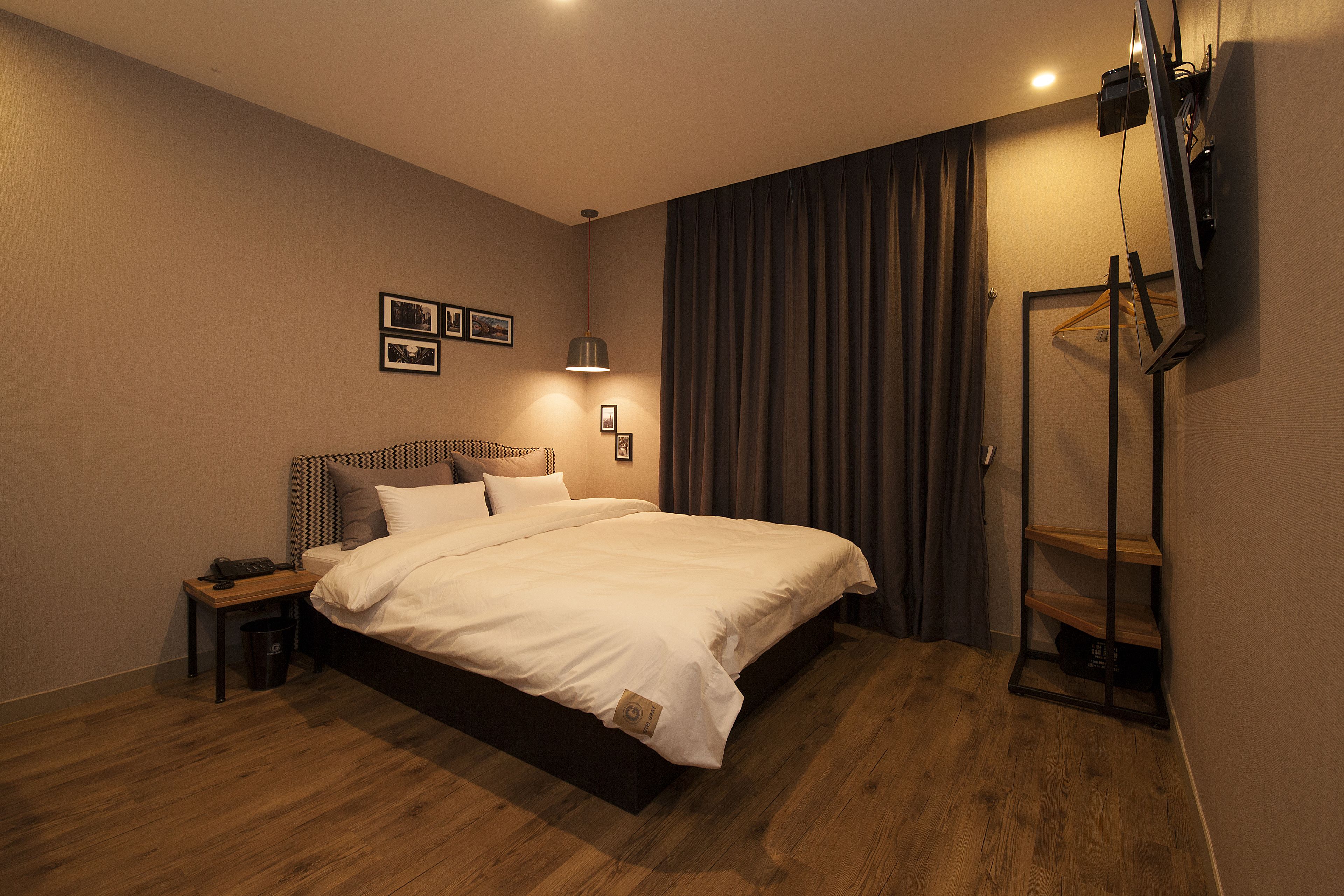 A neatly arranged hotel room with a large bed, bedside tables, a TV mounted on the wall, and a wooden floor.