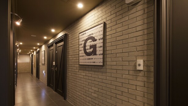 A hallway with a brick wall, a large 'G' sign, and doors leading to rooms. - Hotel Gray (Changwon)