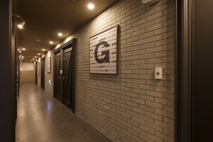 Un pasillo con pared de ladrillo, un letrero grande con la letra 'G' y puertas que dan a varias habitaciones.